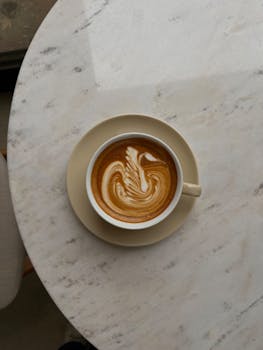 Top-down view of a cappuccino with delicate latte art, served on a marble table.