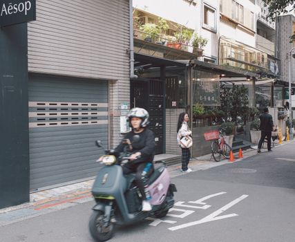 A bustling city street with scooter, pedestrians, and storefronts, capturing the essence of urban life.