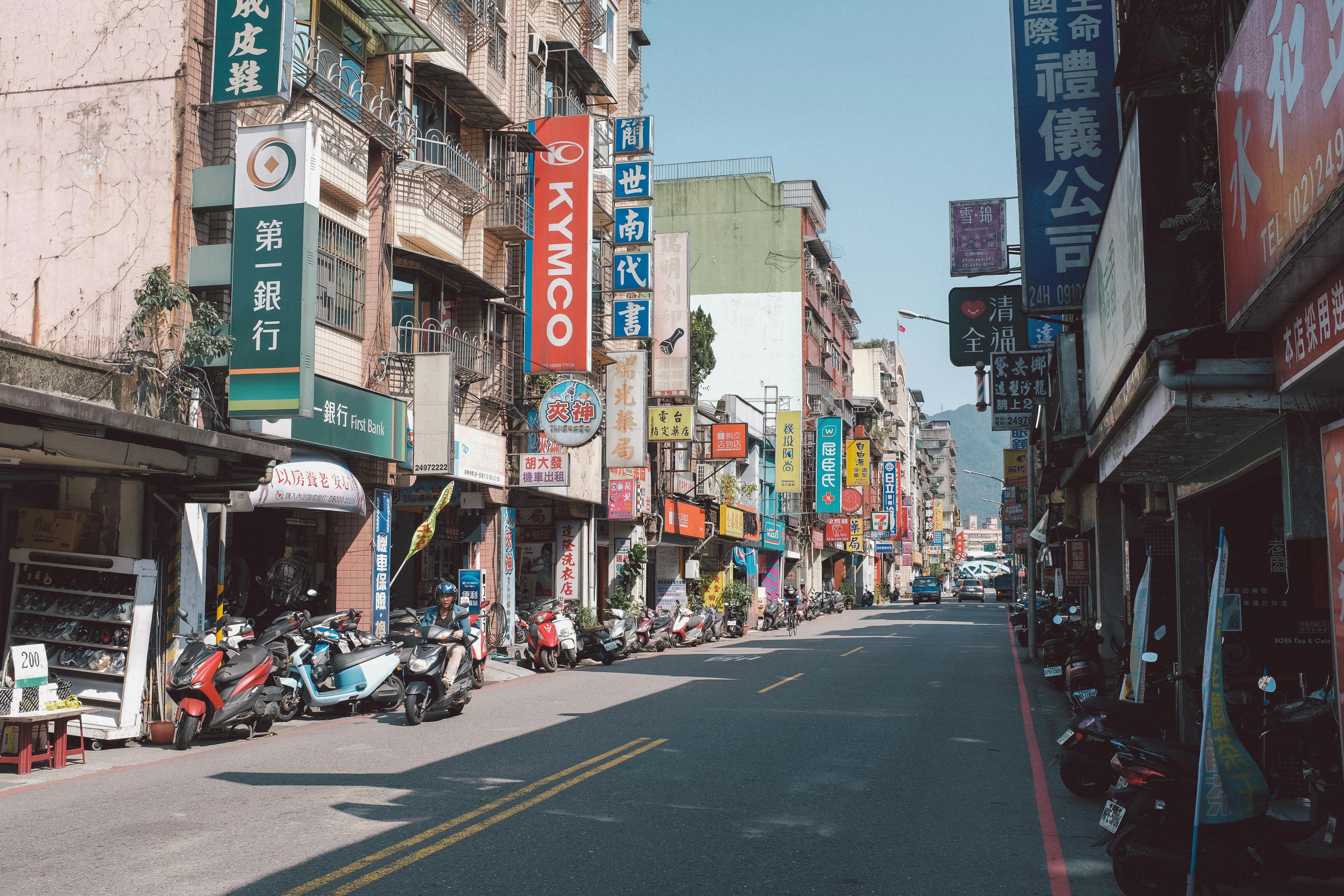Bustling Asian street with vibrant signs and scooters lining the road.