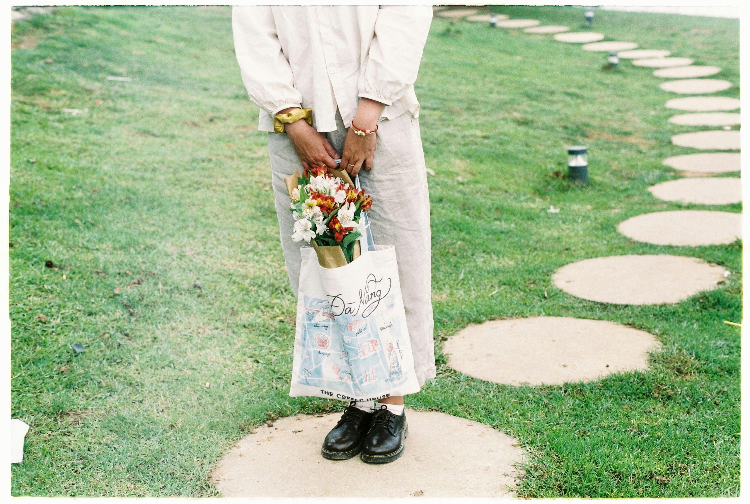 Woman holding a bouquet in a bag standing on garden stepping stones.
