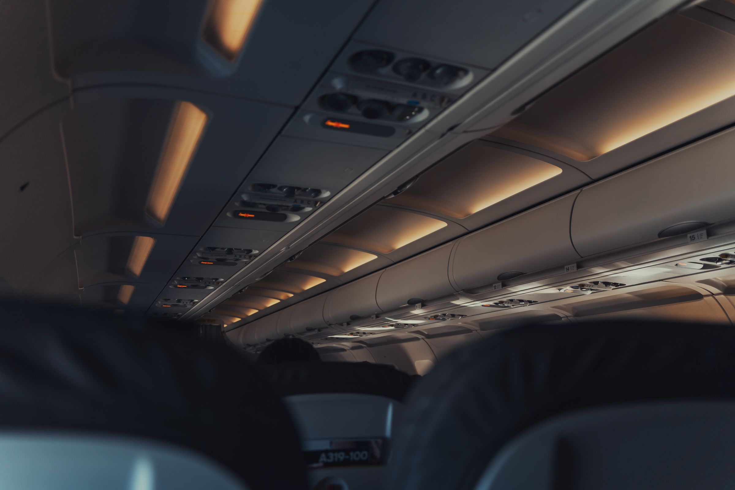Commercial airplane cabin interior, overhead lights and seats in subdued lighting