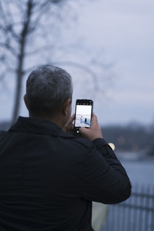 Free Elderly man takes a photo of city scene with smartphone. Evening urban setting. Stock Photo