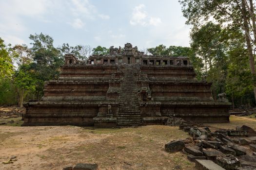 A stunning ancient temple with weathered stone steps surrounded by lush trees and a blue sky.