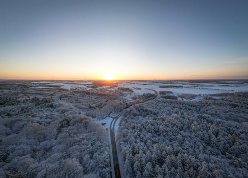 A stunning aerial winter landscape of Spier, Nederland at sunset, capturing snow-covered forests and roads.