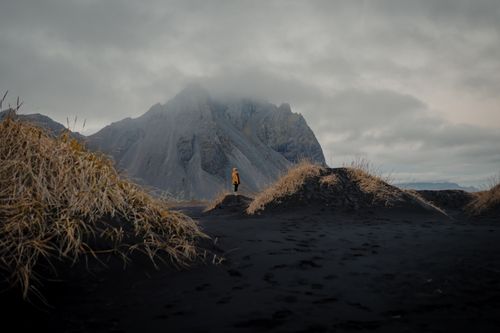 Free A solitary figure stands against a dramatic Icelandic mountain under a cloudy sky. Stock Photo