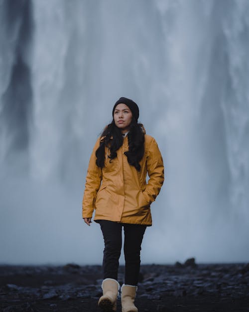 Photo of a Brunette Woman Wearing Yellow Raincoat, and Waterfall in Background