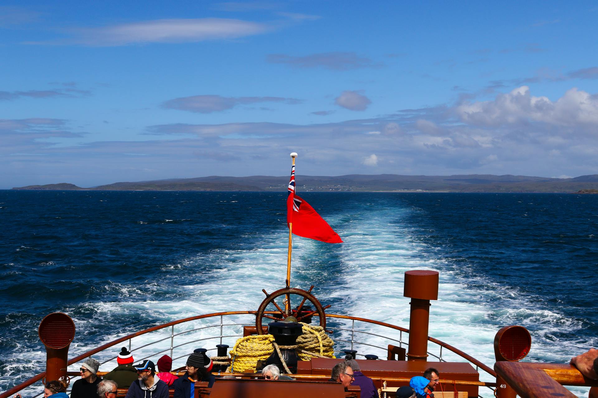 Cruise ship deck view with flag, ocean waves, and scenic seascape on a bright day.