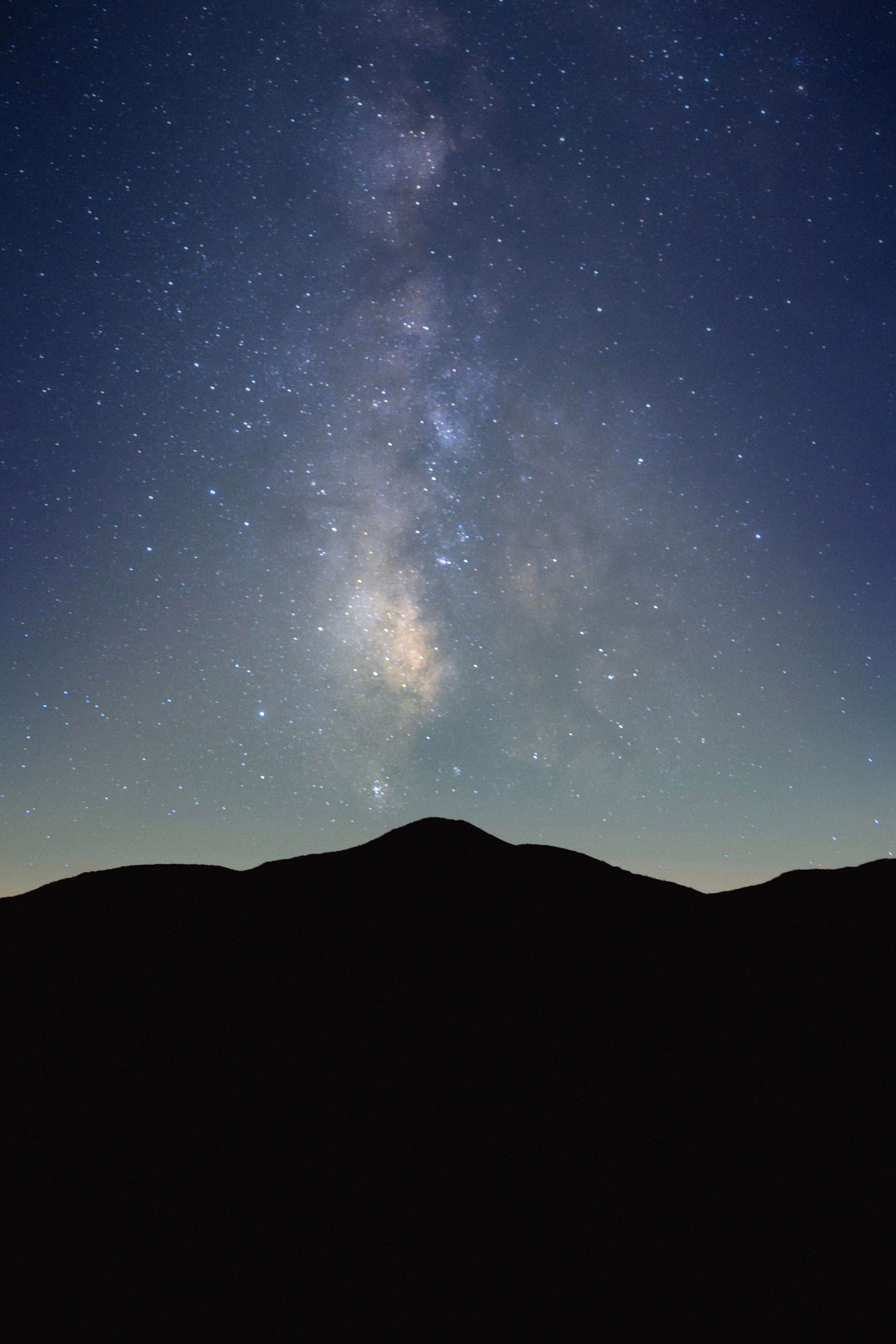 Fotomural Una vista impresionante de la galaxia de la Vía Láctea iluminando el cielo nocturno sobre una silueta de montaña.