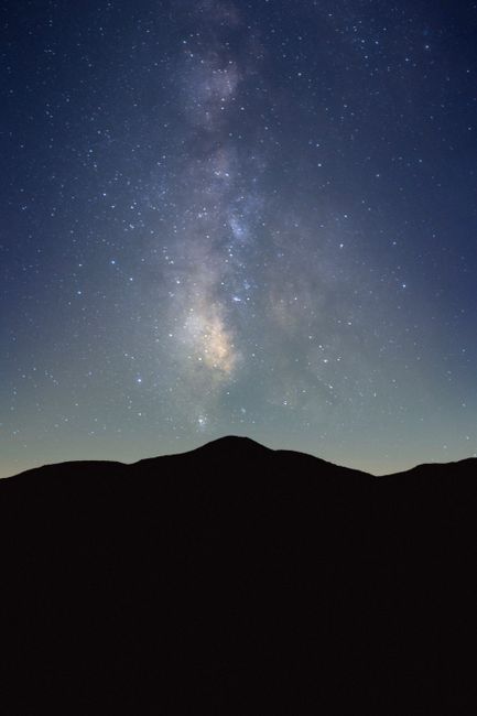 Fotomural Una vista impresionante de la galaxia de la Vía Láctea iluminando el cielo nocturno sobre una silueta de montaña.