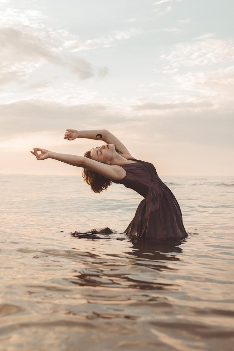 Woman In Dress Dancing In Sea On Sunset