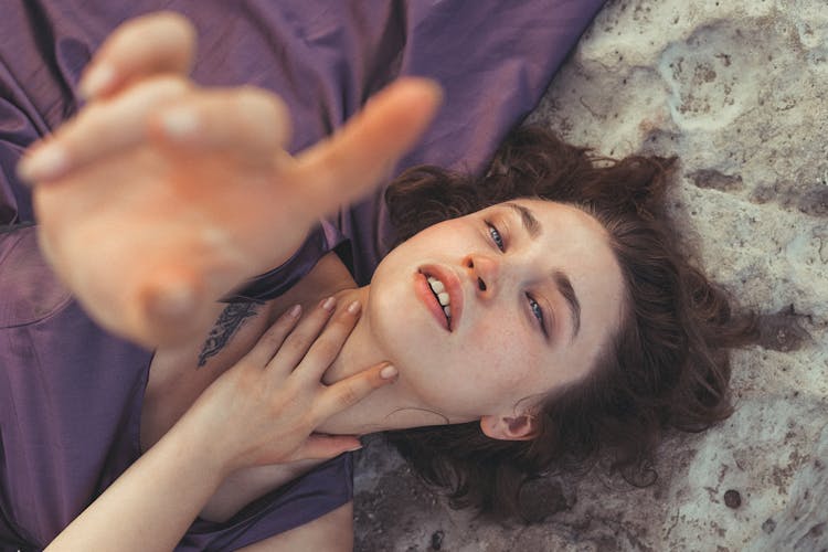 Close-up Of Woman Lying On Sand Beach Stretching Hand To Camera