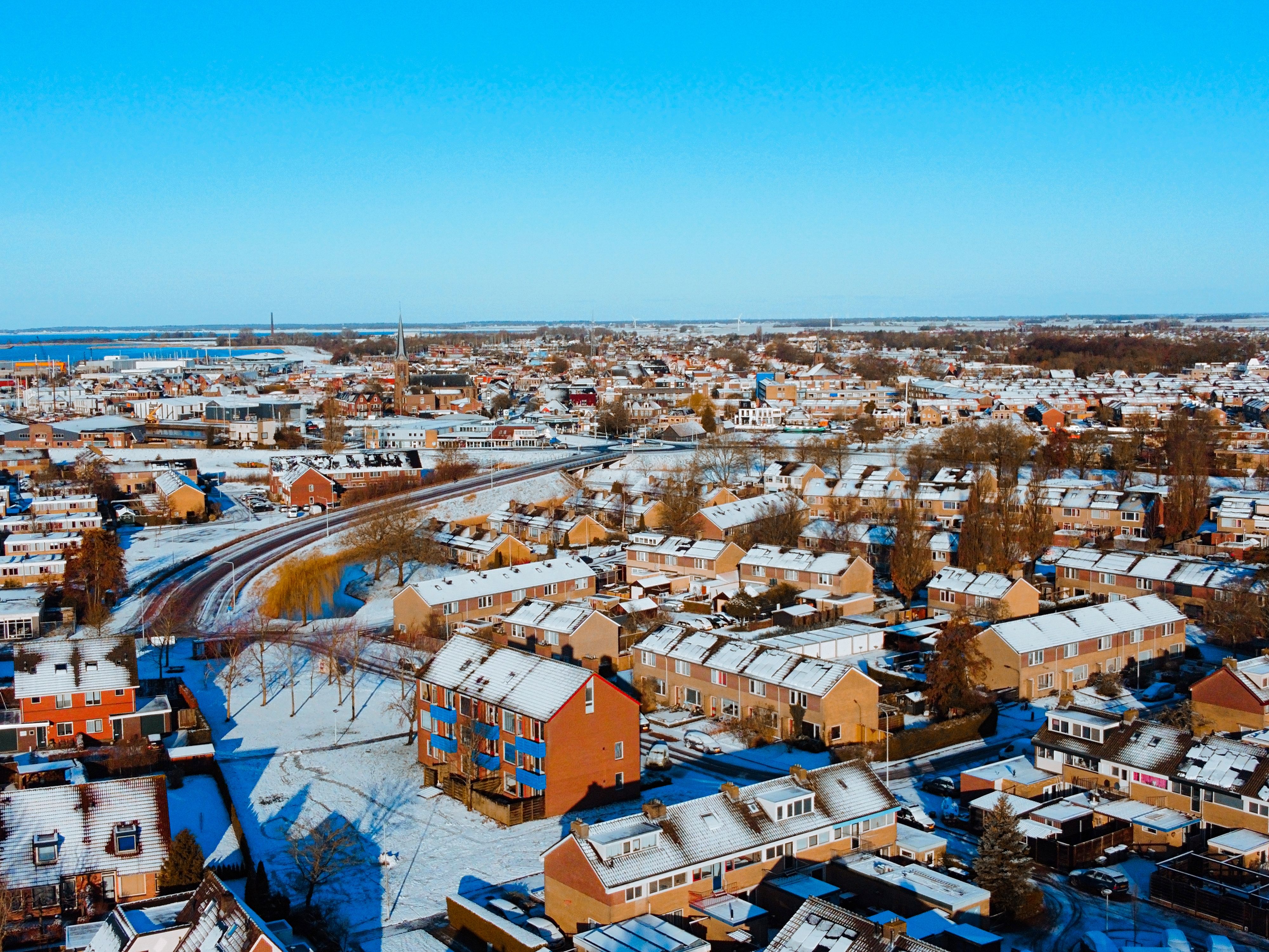 Aerial view of a snow-covered urban landscape showcasing houses and city skyline under a clear blue sky.