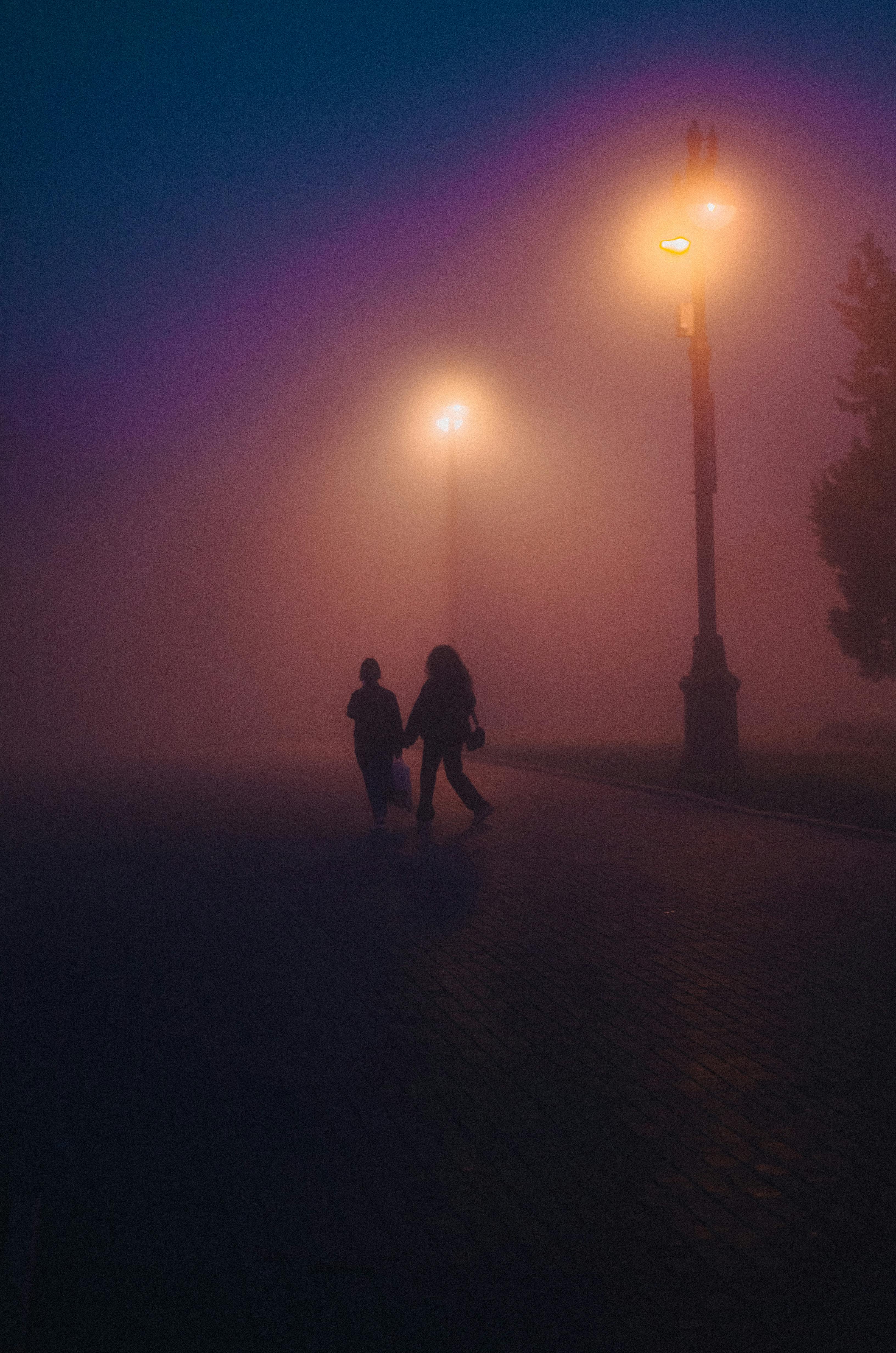 Silhouettes of pedestrians walking under street lamps in Baku, Azerbaijan's thick evening fog.