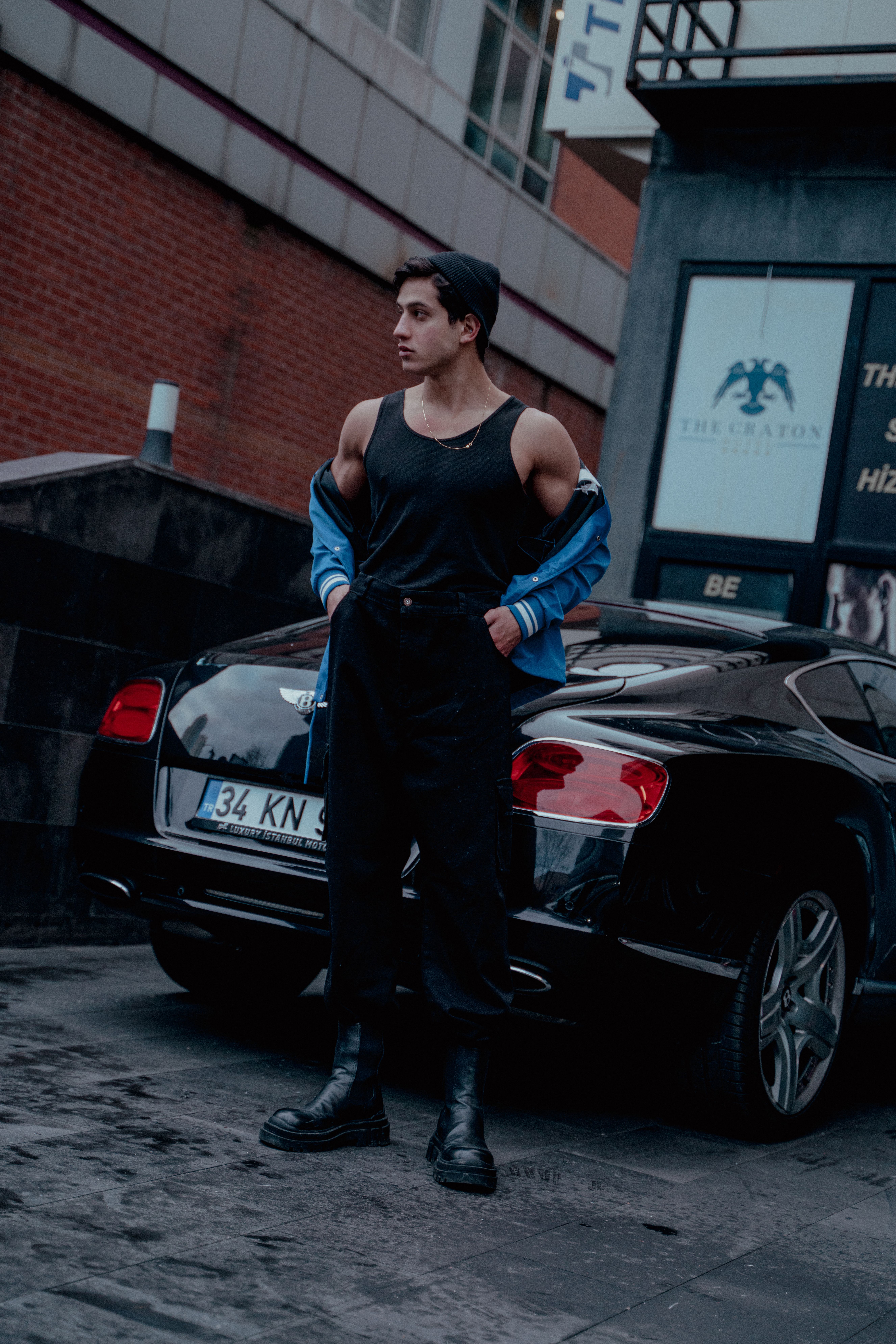 Stylish man in urban Istanbul poses with a luxury car, showcasing modern street fashion.
