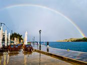 Breathtaking view of a rainbow spanning over Lagkada's seaside promenade, with reflections on wet paths.