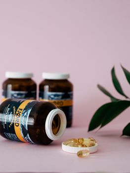 Fish oil capsules in bottles on a soft pink backdrop, perfect for health and wellness themes.