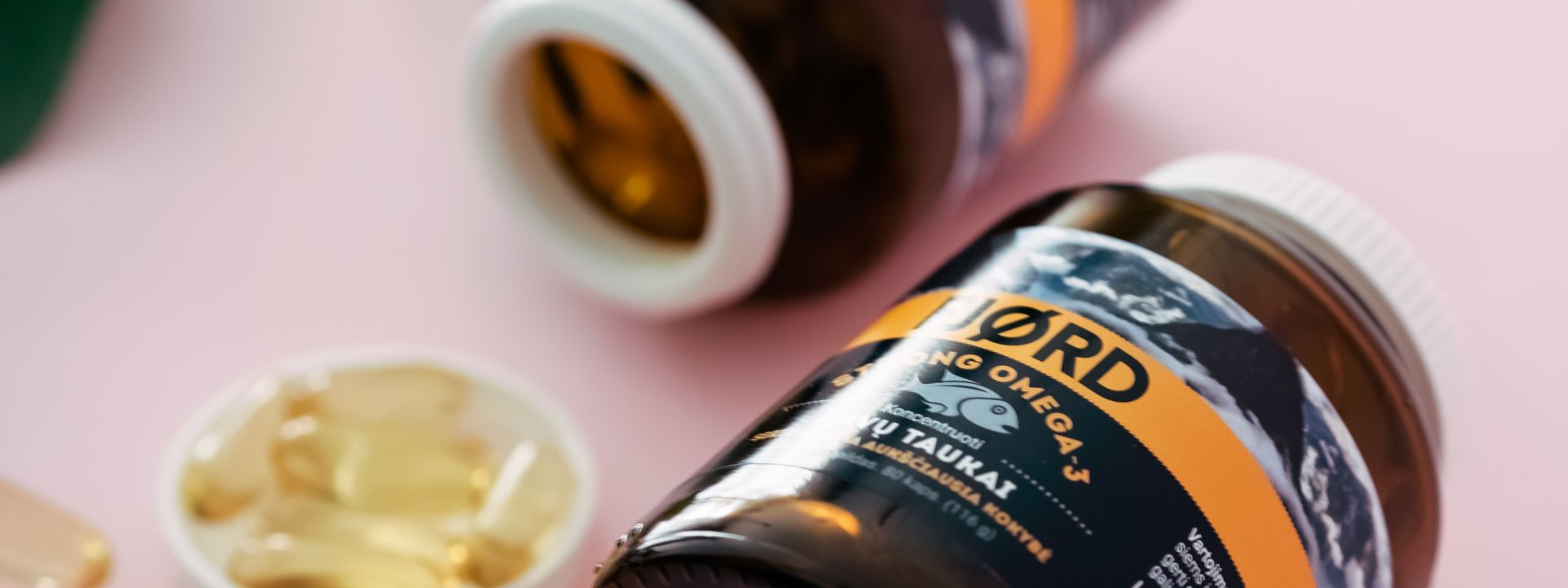 Omega-3 supplement bottles and softgels on a soft pink wellness background