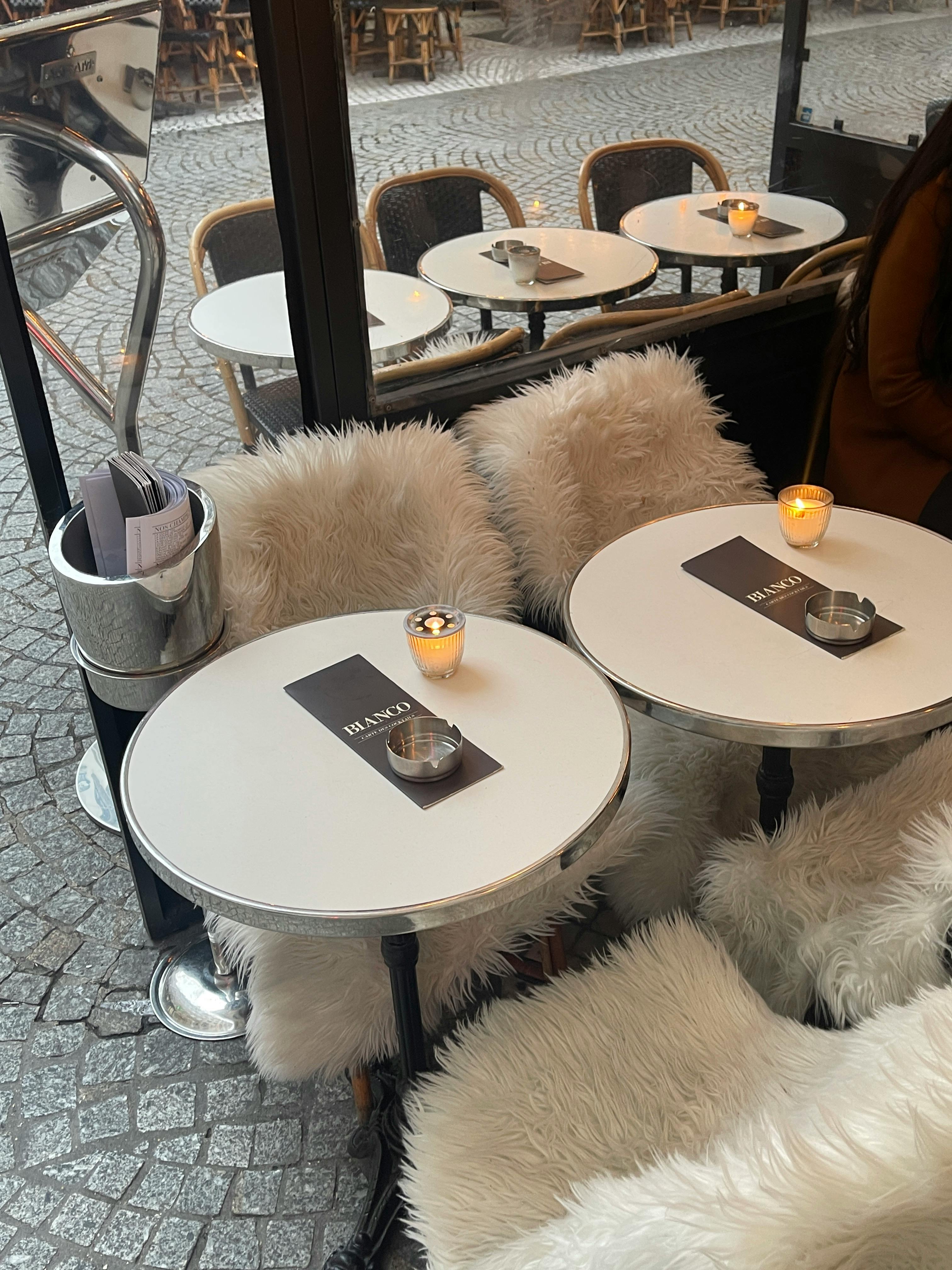 Charming outdoor café with fur adorned chairs and minimalistic tables.