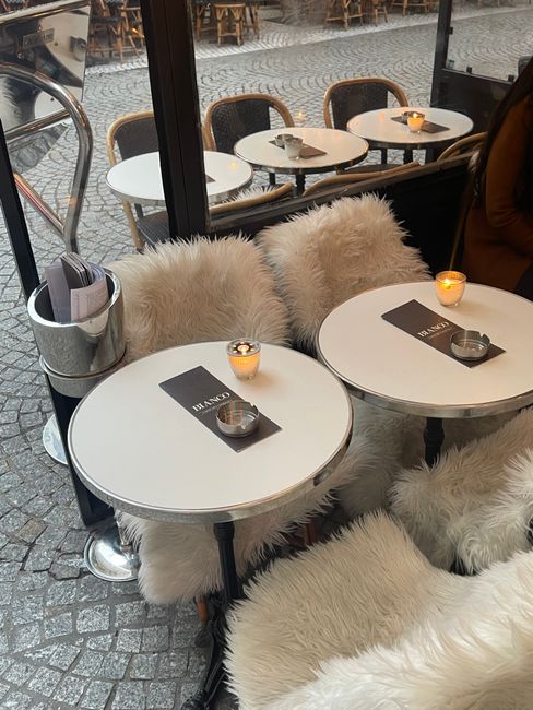 Charming outdoor café with fur adorned chairs and minimalistic tables.