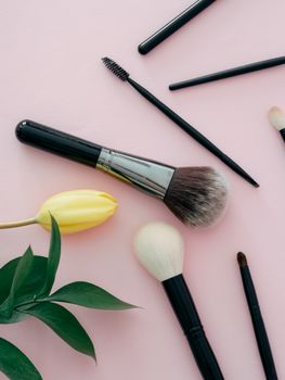 Aesthetic flat lay of makeup brushes and a yellow tulip on a soft pink background.