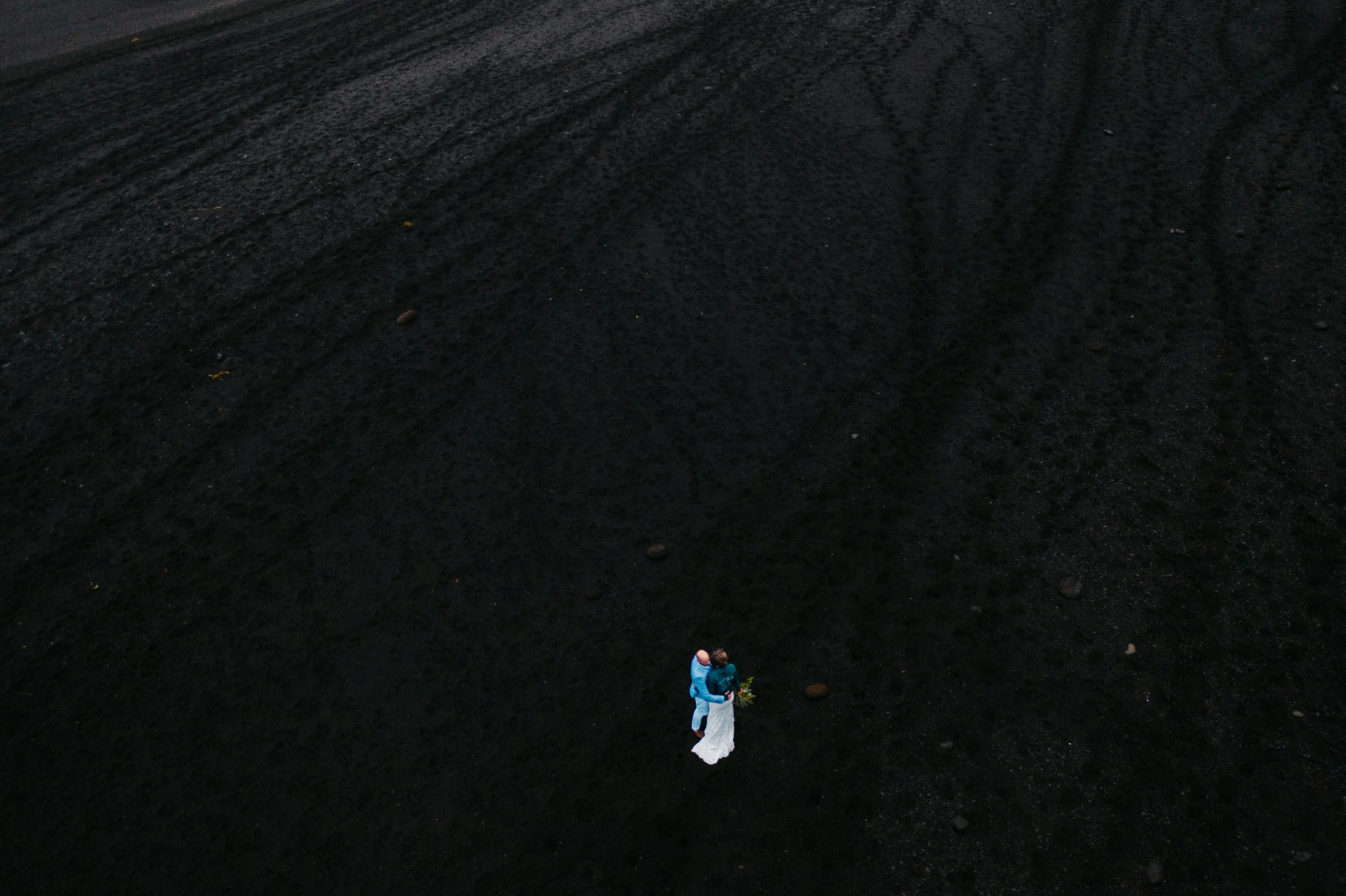 Drone shot of a couple embracing on Iceland's volcanic black sand beach in Vik, Mýrdalshreppur, highlighting romance and nature.