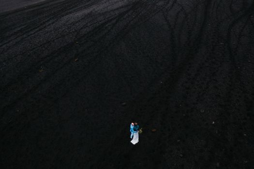 Drone shot of a couple embracing on Iceland's volcanic black sand beach in Vik, Mýrdalshreppur, highlighting romance and nature.