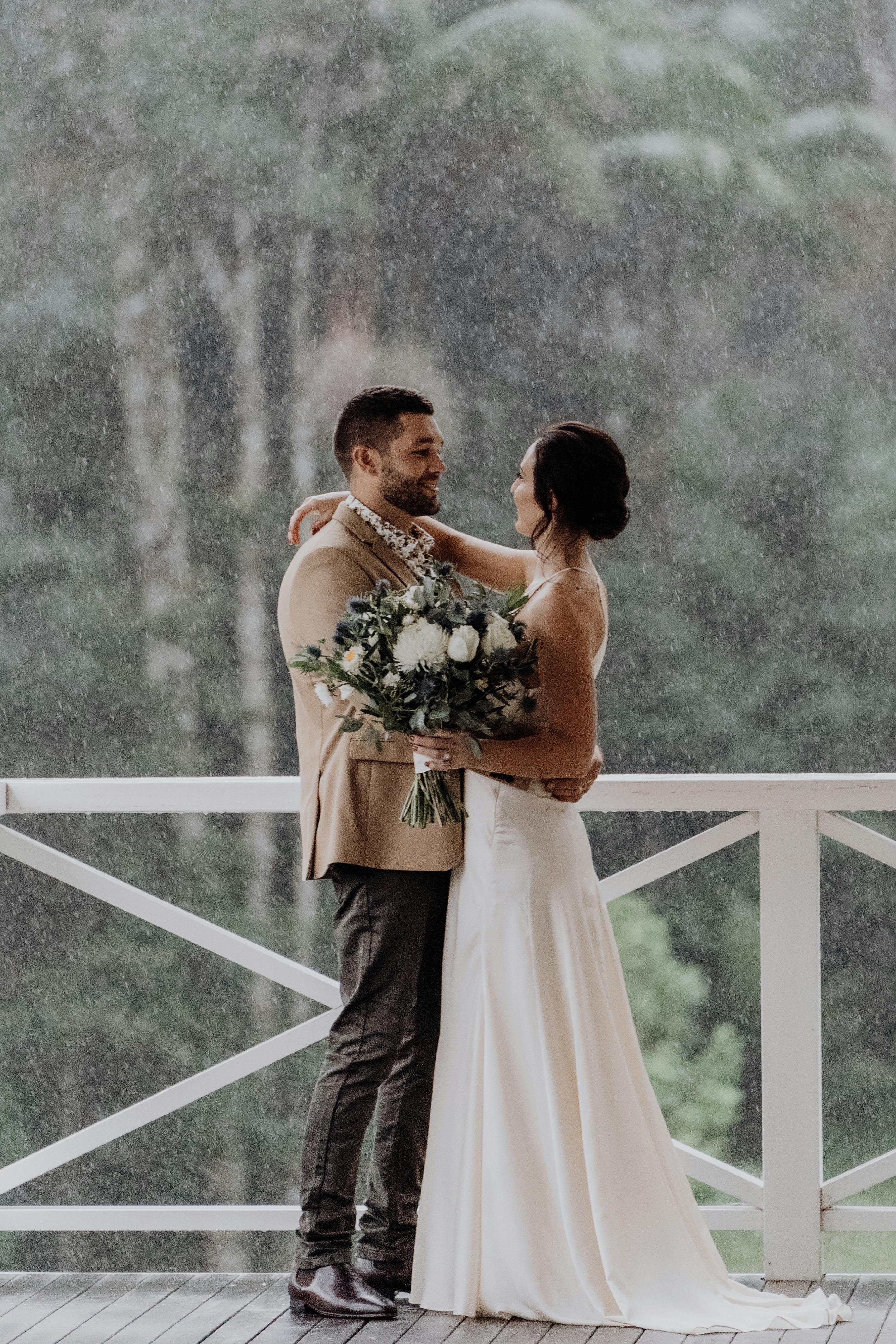 A couple embraces during a rainy wedding ceremony at a Byron Bay terrace.