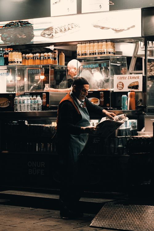 Free Senior man reads paper at a vibrant street food stall in the evening. Stock Photo