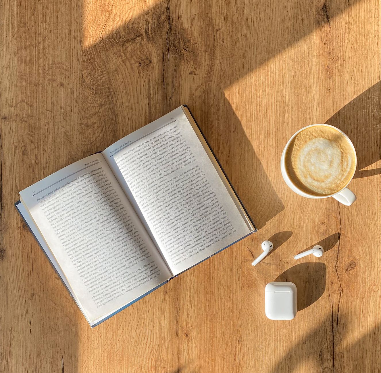 Top view of an open book with coffee and wireless earphones on a wooden table, capturing a cozy reading atmosphere.