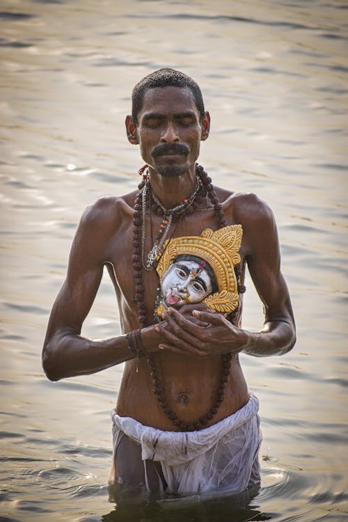 Free Man Holding Kali Mask and Taking Ritual Bath in Ganges River Stock Photo