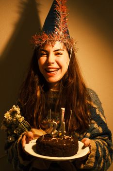 Smiling woman wearing a party hat, holding a birthday cake with '24' candles, creating a festive mood.