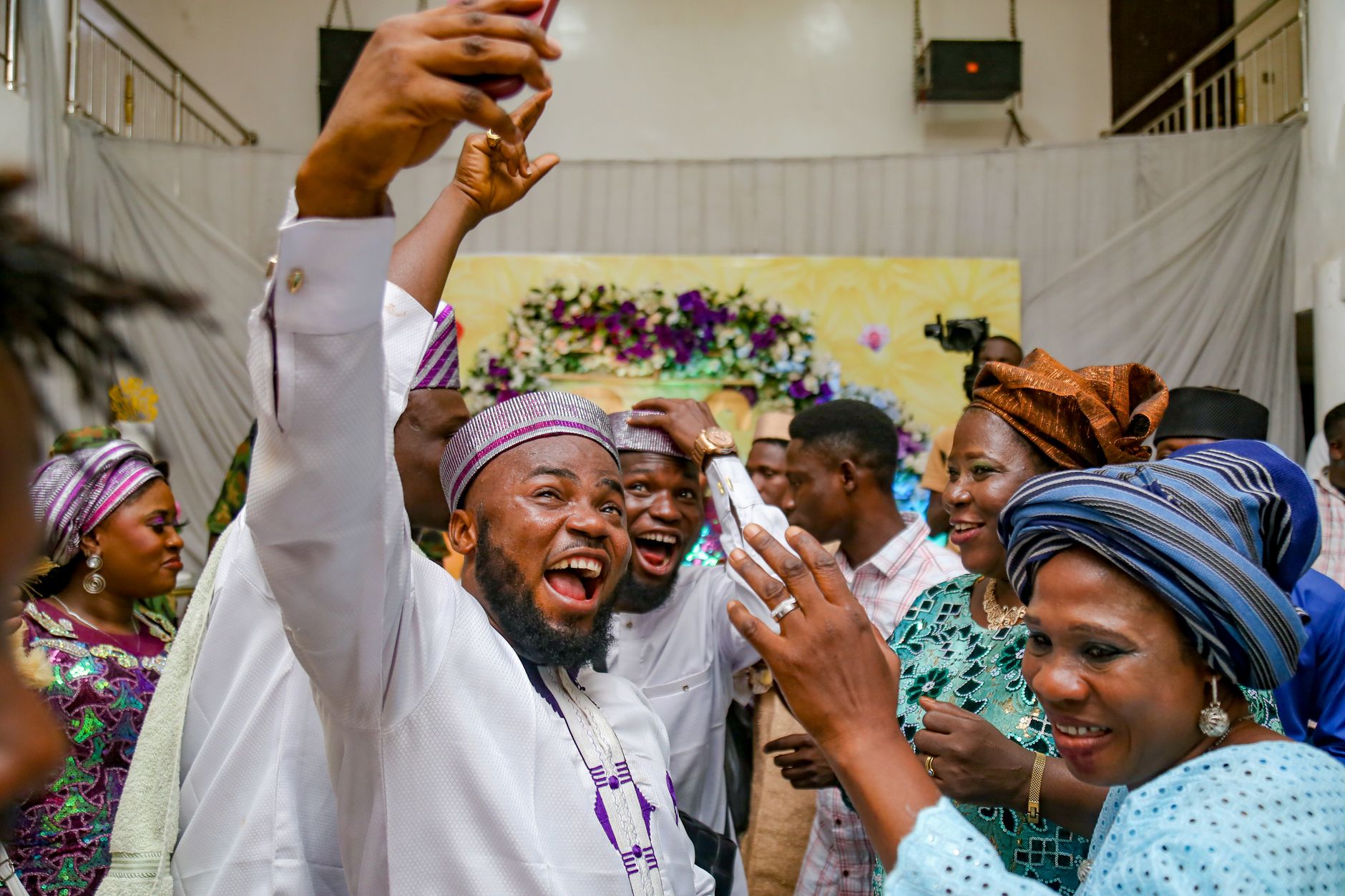 Group of adults celebrating in vibrant traditional Nigerian clothing indoors.