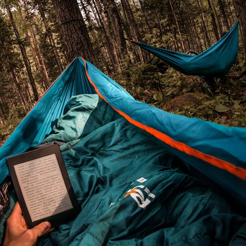 Free Person Holding Amazon Kindle While Lying on Hammock Beside Other Camper
 Stock Photo