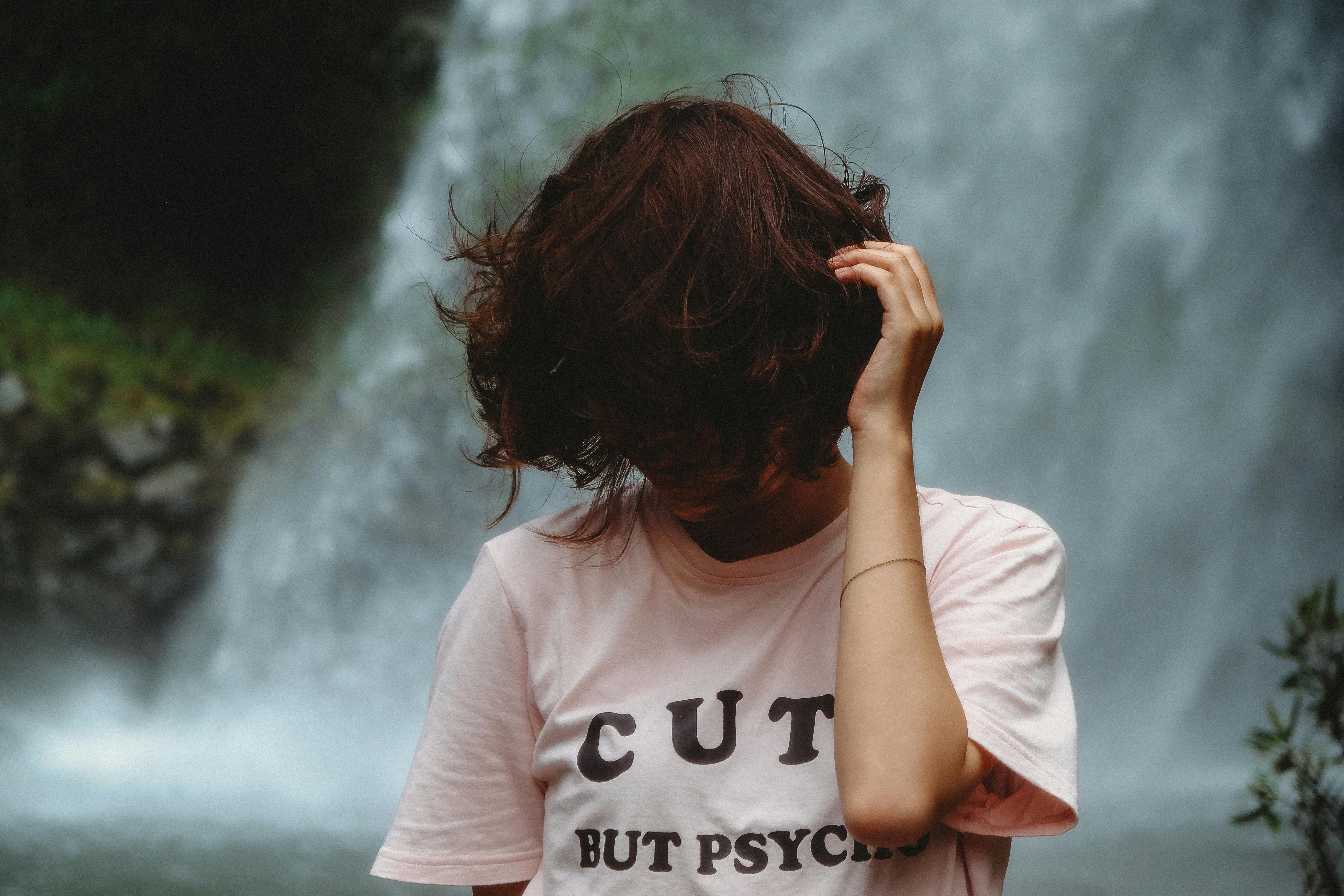 一名女子站在瀑布旁，头发遮住了脸