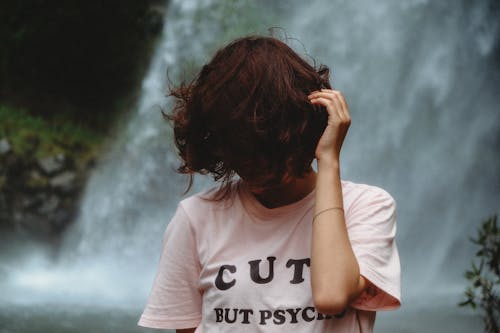 Woman Standing Looking Down While Holding Hair Near Waterfall