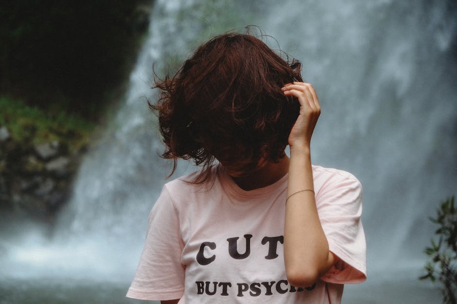 Woman standing by a waterfall with hair covering her face. Casual outdoor portrait.