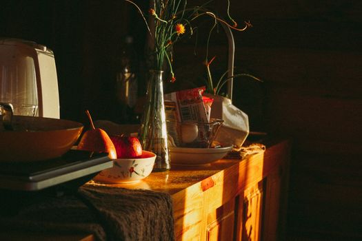 温暖的阳光照亮了质朴的厨房柜台，苹果、梨和一瓶鲜花摆在上面，营造出舒适的氛围