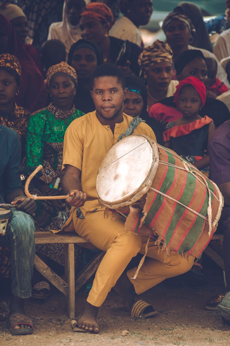 Man Sitting On Bench Among Crowd Playing Drum