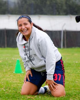 A cheerful teenager in sportswear kneeling on a field, showcasing joy and relaxation.