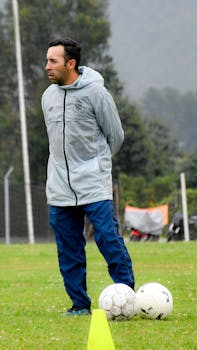 Soccer coach on field with training balls, wearing sportswear and observing.