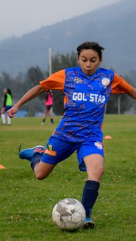 A determined young girl in colorful soccer attire takes a powerful shot on an outdoor field.