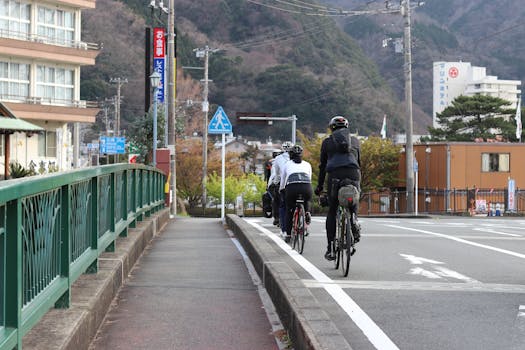 Group of cyclists riding through the streets of Itō, Shizuoka, Japan, with scenic mountain backdrop.