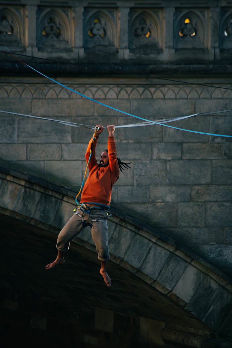 Man Hanging From Rope By Bridge