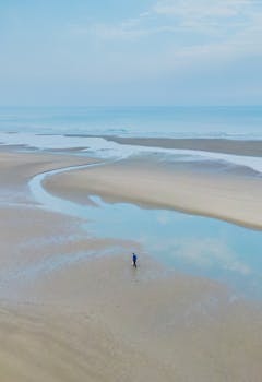 A serene beach scene with a single person walking along the vast sand dunes under a blue sky.