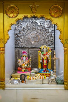 Colorful Hindu temple shrine featuring Ganesh idol adorned with flowers, showcasing traditional Indian art.