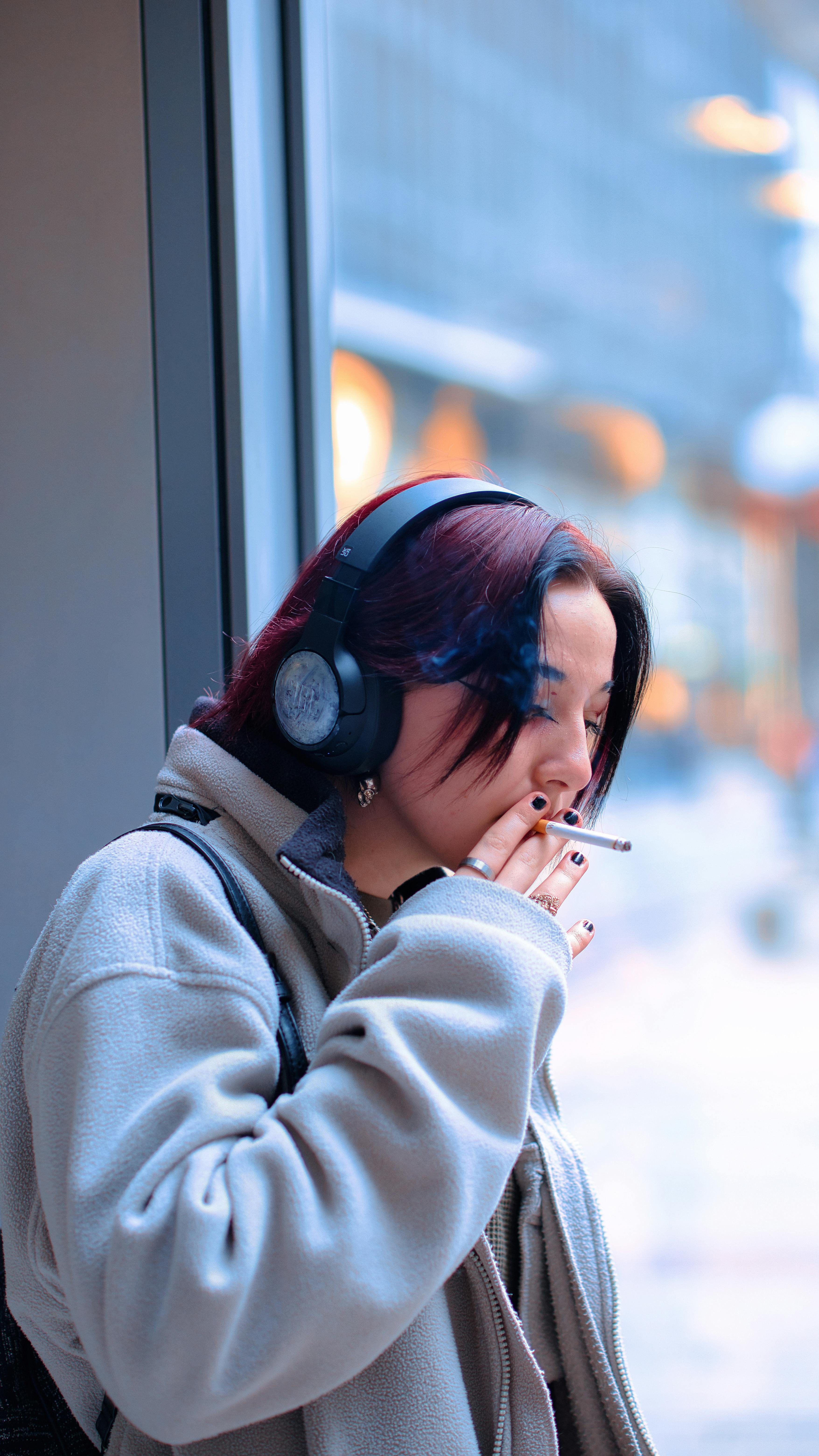 Young Woman in a Fleece Sweatshirt and Headphones Smoking a