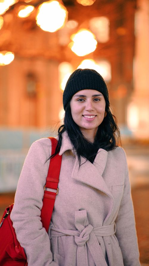 Free A woman in a winter coat smiles warmly, illuminated by city lights. Stock Photo