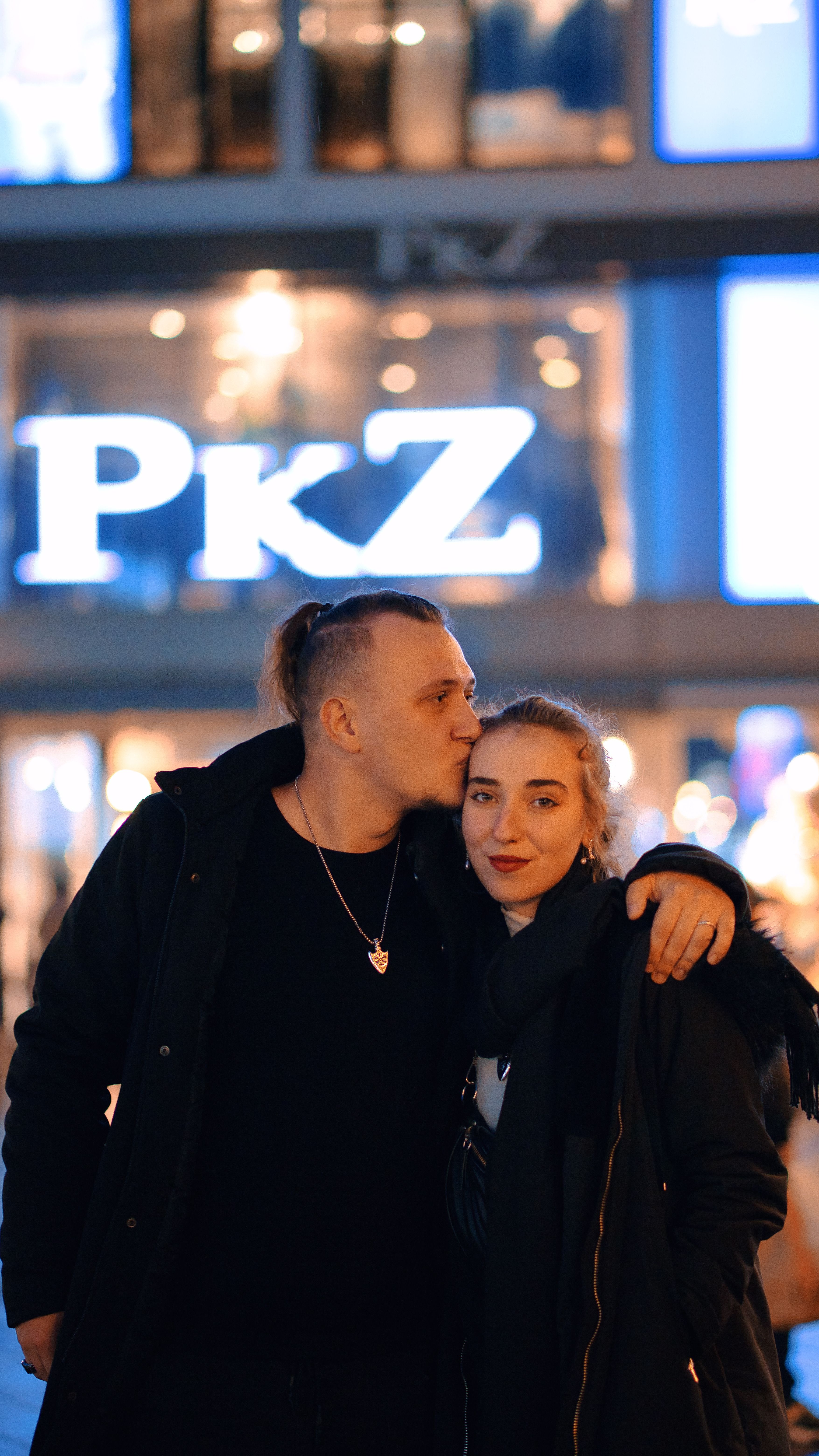 A couple in cozy outerwear shares a tender moment during a city night outing.
