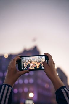 Hands hold a smartphone capturing a crowd in Mexico City at twilight.