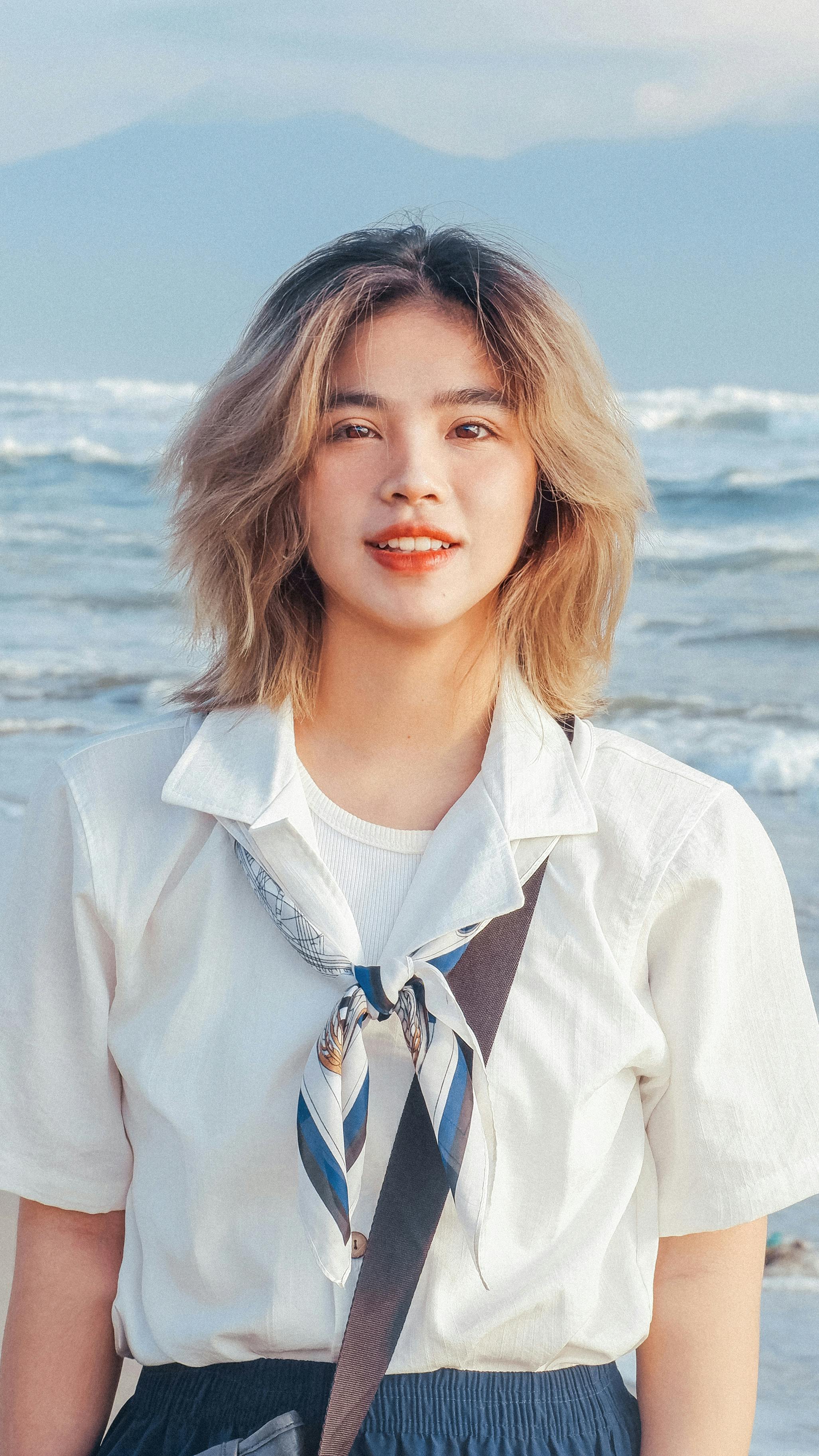 Teen girl smiles in white shirt and scarf with ocean waves in the background.